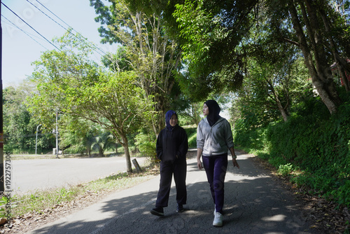 Wallpaper Mural Two young Muslim women walking together for morning exercise along a green park pathway filled with trees on a bright sunny day.  Torontodigital.ca