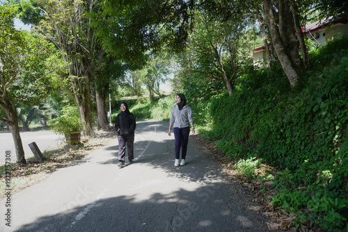 Wallpaper Mural Two young Muslim women walking together for morning exercise along a green park pathway filled with trees on a bright sunny day.  Torontodigital.ca