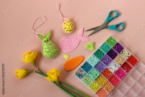 Easter decoration with eggs, hand made bunny, colorful seed beads and daffodils on pink background