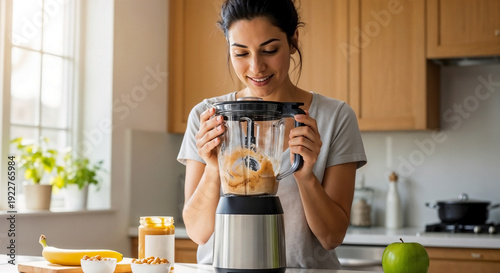 Woman making nutritious peanut butter smoothie in home kitchen. She adds peanut butter, banana, apple to blender, crafting healthy peanut butter smoothie. Perfect for diet plans, wellness blogs.