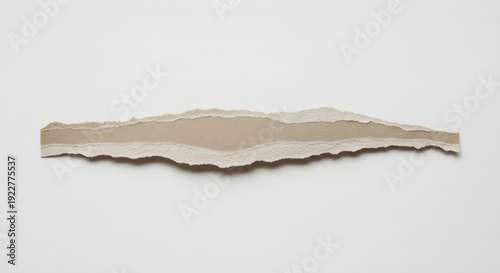Torn beige paper strip with rough edges and layered texture on white background surface