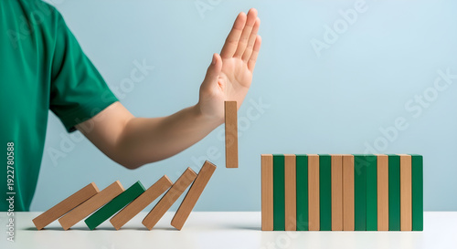 Person intervening to stop domino effect by saving falling wooden blocks from crashing down