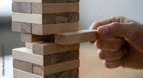 Hand carefully removing wooden block from precarious jenga tower structure game play strategy