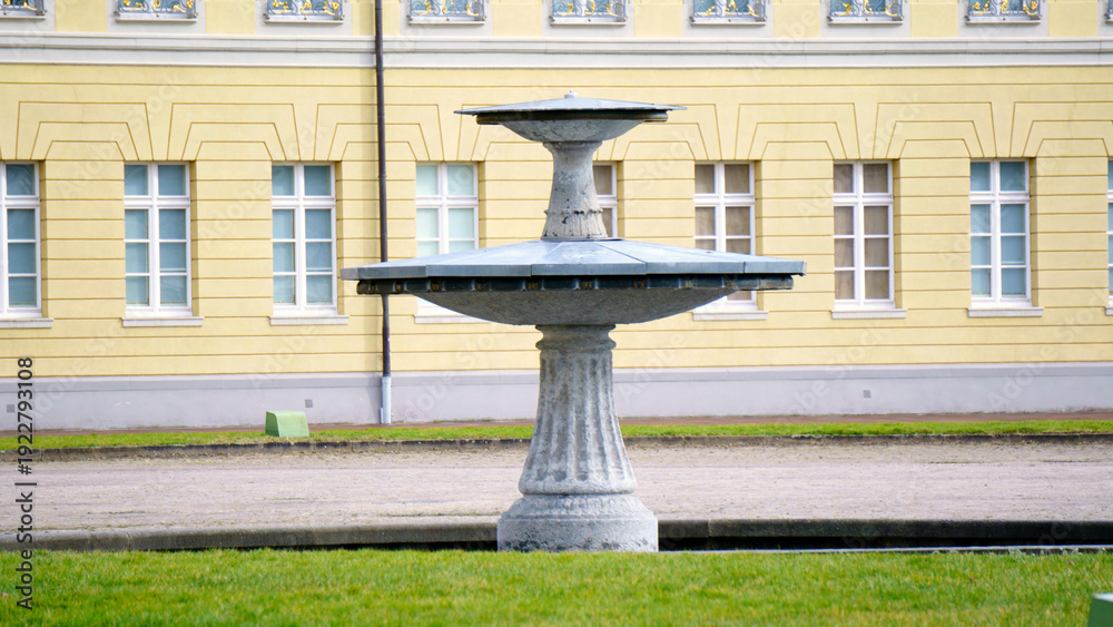 Obraz premium Elegant stone fountain with cascading water flows stands as a park centerpiece. Sculpted details and gentle splashes create a soothing sound amid surrounding greenery. Soft daylight reflects on rippli
