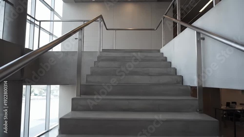 Wide concrete stairs ascend with metallic railings inside a modern building