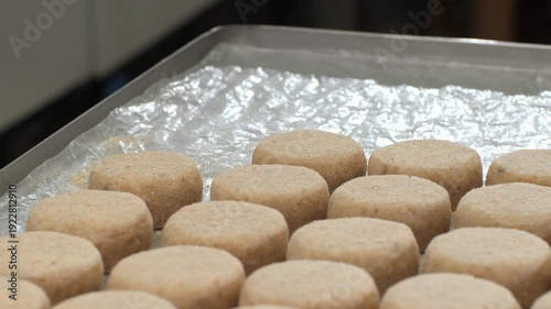 Fresh fish patties put on tinfoil-lined tray while cook lightly presses with flat spatula creating smooth rounded form. Gentle steady motion ensures uniform shape supporting efficient production