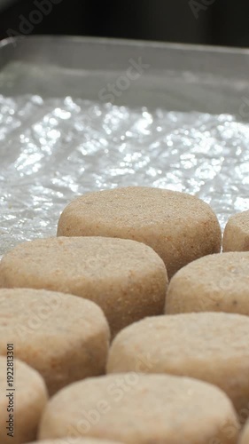 Vertical video. Fresh fish patties put on tinfoil-lined tray while cook lightly presses with flat spatula creating smooth rounded form. Gentle steady motion ensures uniform shape supporting production