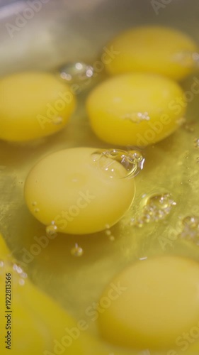Vertical video. Rich egg yolk and clear glistening white drop into deep metal bowl forming silky base for future dough preparation. Smooth texture begins flavorful process supporting baking of bread