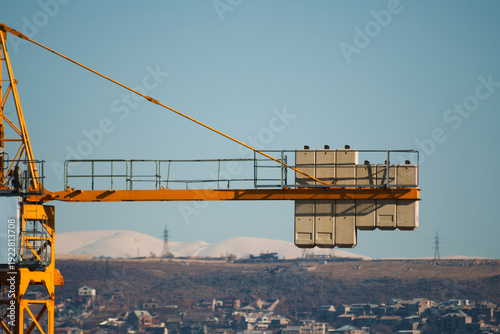 Yellow tower crane against the backdrop of the city from a close distance, The rear part of the tower crane is a console or counter-jib, reinforced concrete or metal counterweight slabs. High quality