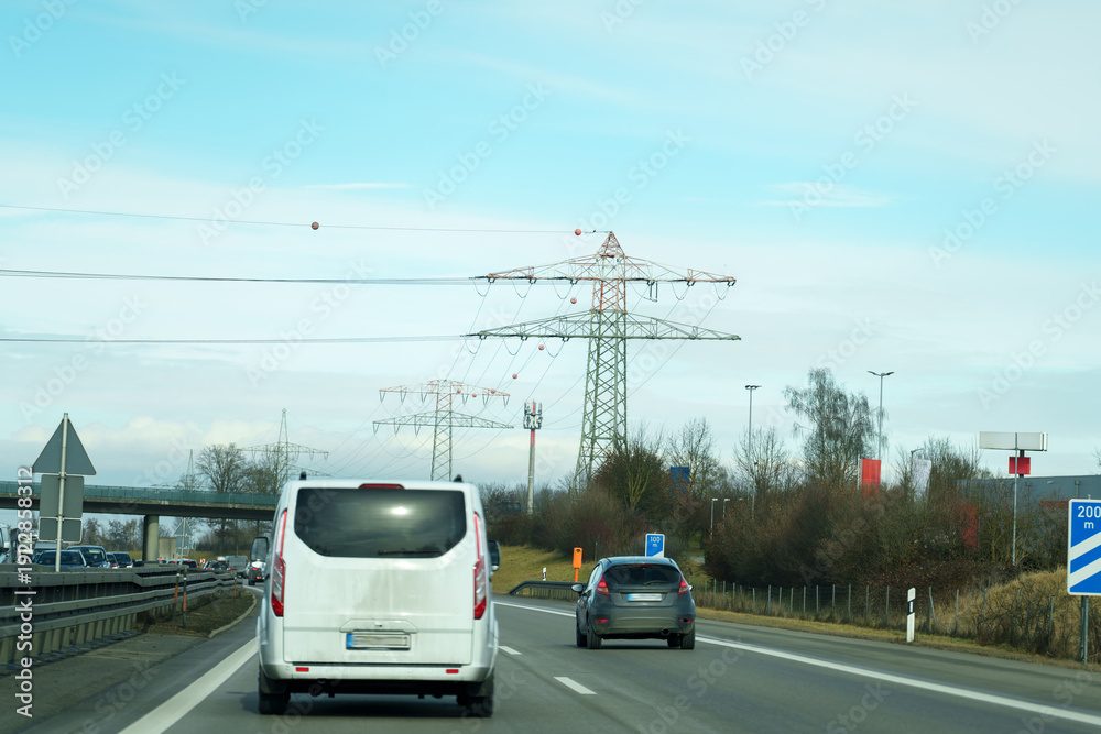 Obraz premium Cars drive on a highway near power lines and road signs in clear weather in a rural area during the day