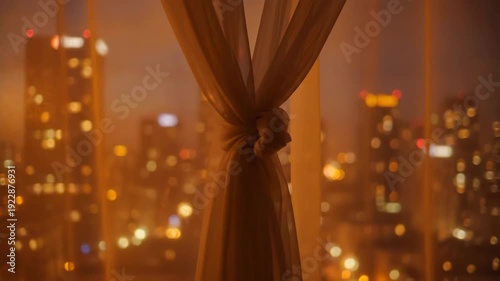Sheer curtain tied in a knot frames a blurry city skyline at night. Warm, glowing lights create a cozy, intimate atmosphere.