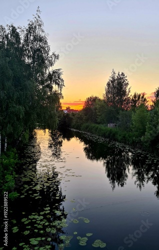 Beautiful sunset on cloudless sky and reflections of trees on smooth surface of water in the river