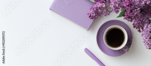 Flat lay of purple coffee cup lilac flowers and notebook on white background with copy space