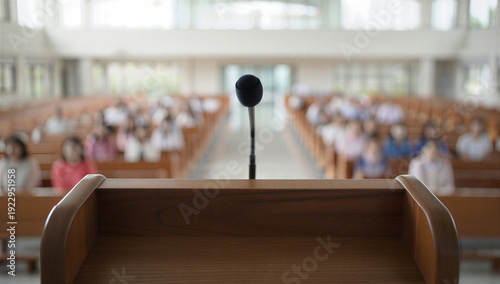 Wooden podium with microphone in large auditorium, empty lectern for public speaking, blurred audience sitting in church pews or lecture hall