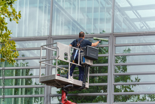 Quadro su tela Worker cleaning large glass facade using lift platform outside modern office bui