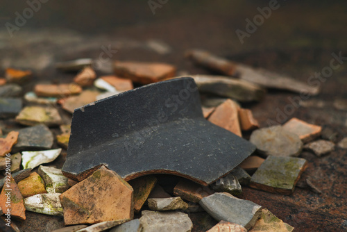 Εκτύπωση καμβά Macro shot of a prominent dark grey ceramic shard lying on a pile of various broken terracotta and clay pottery fragments