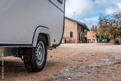 Modern caravan trailer parked on gravel near an old building on a cloudy day, representing travel and nomad life