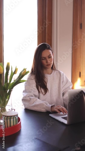 Focused young woman working on laptop at home office, serious female freelancer typing on keyboard and looking at screen, calm lady entrepreneur or student studying online in cozy bright interior