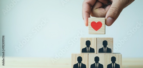 A hand places a red heart block atop a pyramid of human resources wooden blocks.
