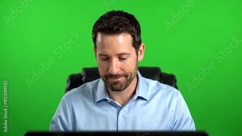 Smiling man in a blue shirt sitting against a green screen background