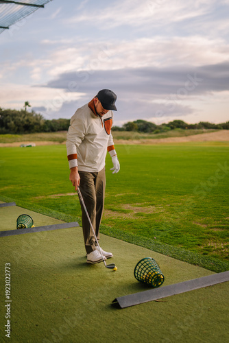 Obraz na plátně Male golfer in white long-sleeve shirt and cap prepares to hit a golf ball at a