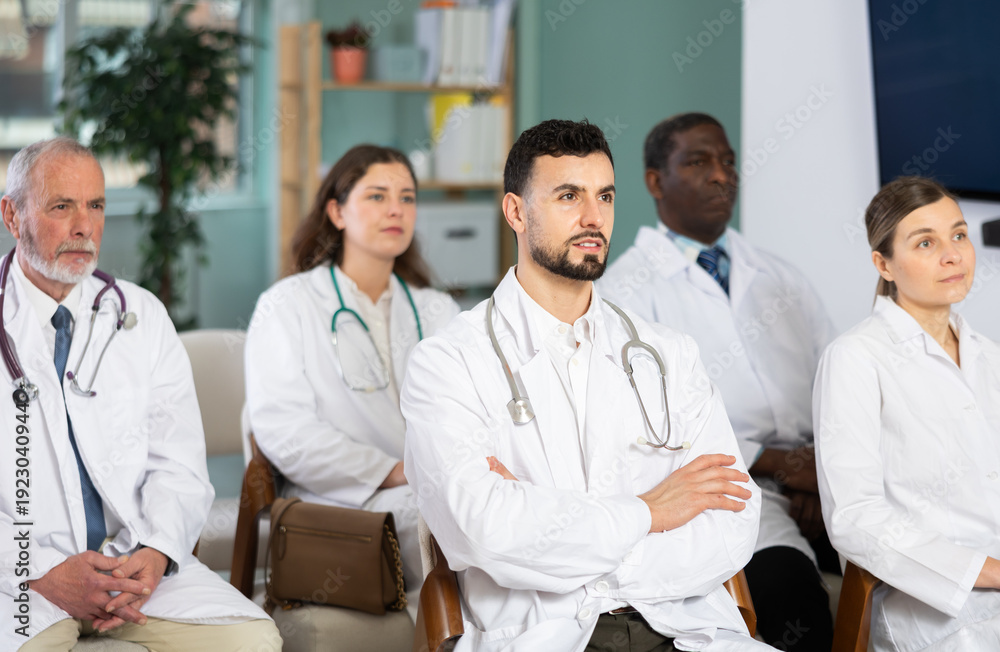 Fototapeta premium Man doctor student at courses meeting listens to teacher and look at speaker. Off-line training in crisis management courses or first aid courses, students listen to lecturer.