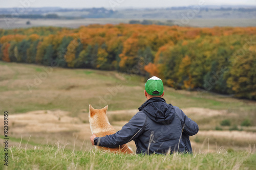 Man sitting with Akita dog on hill overlooking autumn landscape, friendship and companionship concept, horizontal picture with copy space for text