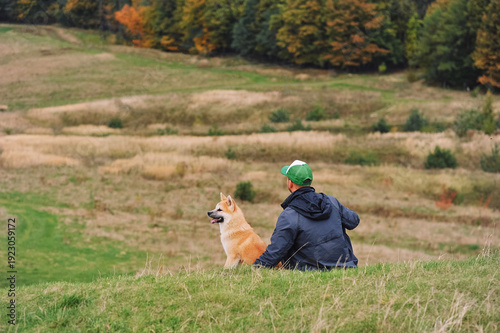 Man sitting with Akita Inu dog overlooking autumn countryside landscape