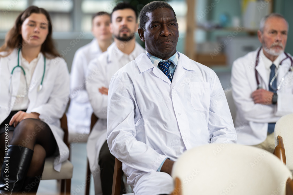 Fototapeta premium Adult male doctor listening to lecture and watching presentation with colleagues in lecture hall