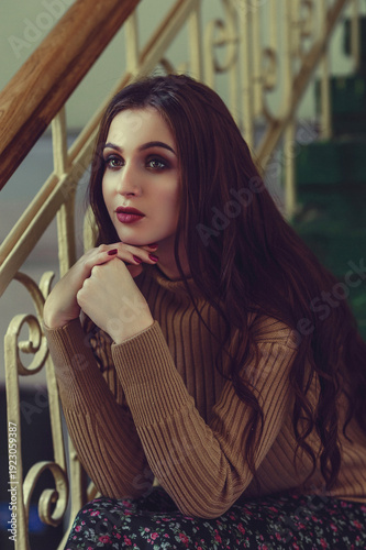 Portrait of stylish young woman sitting on staircase with dramatic makeup