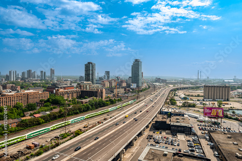 Aerial view showcasing toronto's urban landscape featuring a busy highway, a passenger train on railway tracks, and a distant city skyline under a blue sky