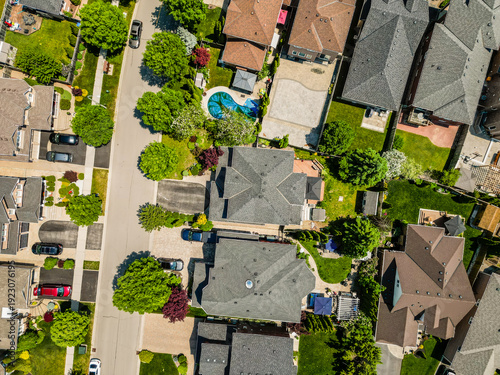 Drone view capturing a well planned suburban residential neighborhood with numerous detached houses. Green lawns. Winding streets. Parked cars. And lush trees. Focusing on modern community development