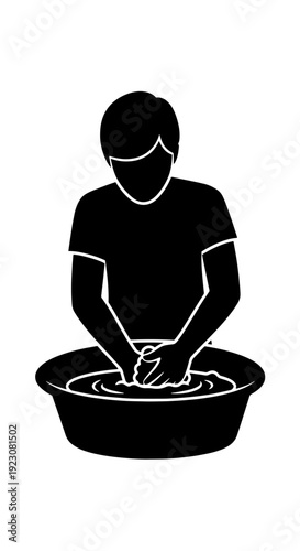 Silhouette of a person washing items by hand in a basin filled with water, performing a manual laundry task.