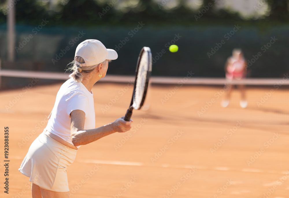 Fototapeta premium Rear view of focused european aged woman playing tennis match in open-air court of tennis club