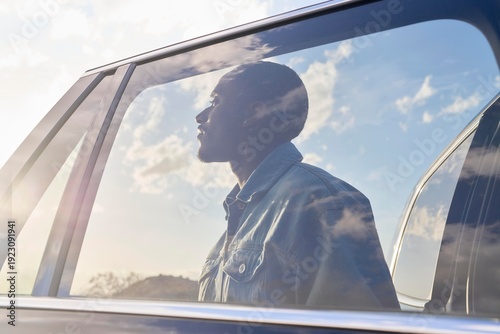 Man gazes thoughtfully outside car window during sunset