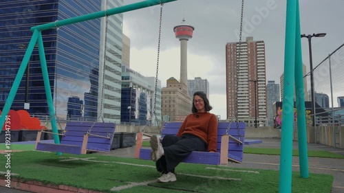 Wallpaper Mural Woman smiling while swinging on a rooftop urban park looking at the cityscape and Calgary Tower Torontodigital.ca