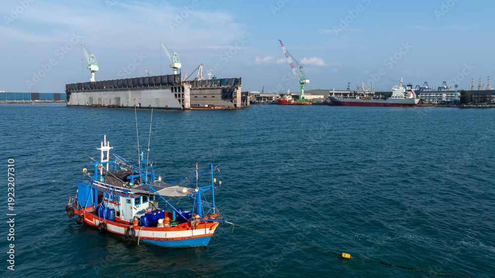 Fototapeta premium Traditional wooden Thai fishing boat with massive industrial and cargo terminal, Contrast and coexistence between local livelihoods and growth modern heavy industry.
