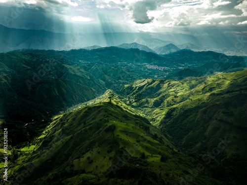 Dramatic aerial drone view of the lush green Andean mountain valleys near Vilcabamba, Loja Province, Ecuador, with spectacular god rays of sunlight breaking through dramatic clouds, illuminating the l