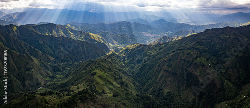 Dramatic aerial drone view of the lush green Andean mountain valleys near Vilcabamba, Loja Province, Ecuador, with spectacular god rays of sunlight breaking through dramatic clouds, illuminating the l