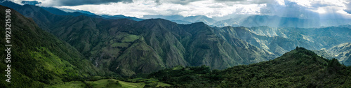 Dramatic aerial drone view of the lush green Andean mountain valleys near Vilcabamba, Loja Province, Ecuador, with spectacular god rays of sunlight breaking through dramatic clouds, illuminating the l