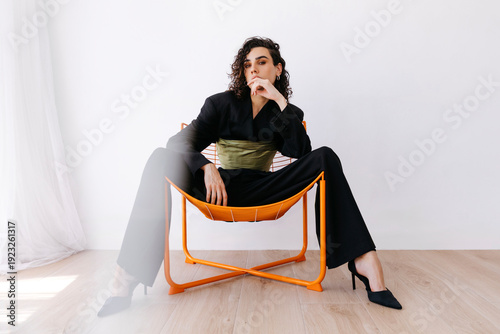 Queer man wearing suit and heels sitting