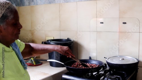 Black woman roasting cacao beans in rustic rural kitchen - Traditional chocolate making process