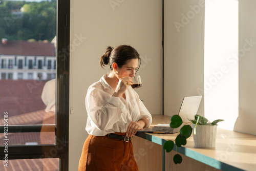 Woman Enjoying Coffee While Working at a Desk in a Bright Room