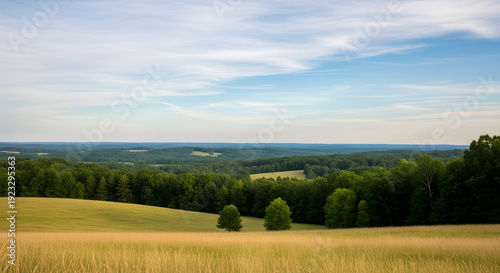 A wide panoramic shot of rolling green hills and lush forests under a soft blue sky during the day