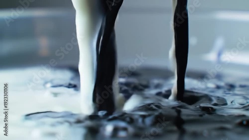 Streams of black and white liquid are poured together, creating a visually striking contrast and dynamic flow.