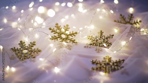 Golden snowflake ornaments are scattered on a white fabric with fairy lights creating a festive and magical atmosphere.