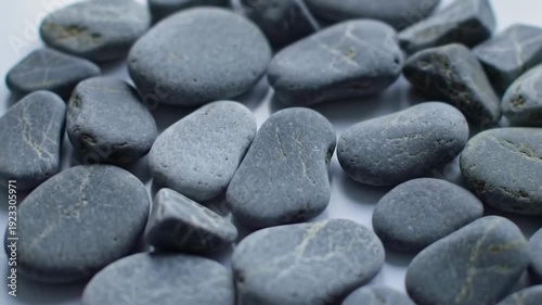 Pile of smooth gray stones are arranged in a circle on a white surface, creating a natural and calming composition.