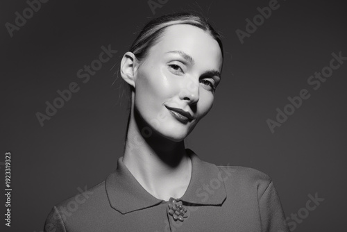 Portrait of a smiling white woman with fair skin and slicked back hair wearing a textured jacket in black and white studio lighting. Concept of elegance, confidence, and fashion.