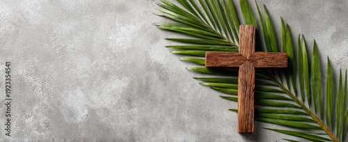A wooden cross and palm leaves lie on a textured, gray surface