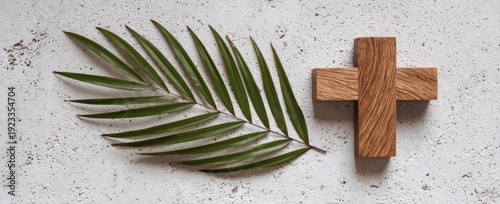 Palm frond next to a wooden cross on a textured off-white surface